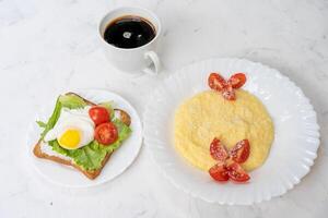 smörgås med friterad ägg sallad och tomat på en vit tallrik på en vit bakgrund. foto