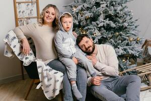 jul familj lycka porträtt av pappa, gravid mamma och liten son Sammanträde fåtölj på Hem nära jul träd kram leende foto