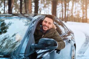 ung attraktiv caucasian man sitter på de hjul av hans bil solig vinter- dag. foto