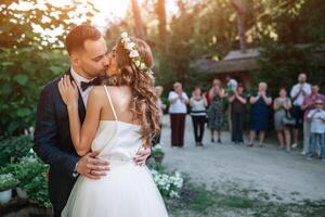 de brudgum kyssar de brud i främre av de gäster på de utgång ceremoni foto