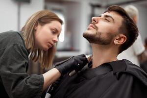ung skön caucasian kvinna frisör nedskärningar skägg stilig man på modern frisör foto