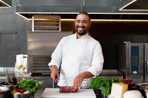 stilig ung afrikansk kock stående i professionell kök i restaurang framställning en måltid av kött och ost grönsaker. foto