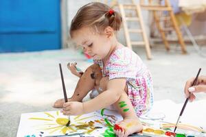 söt liten caucasian flicka njuter målning på de bakgård med papper, vatten Färg och konst borsta. selektiv fokus foto