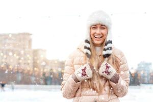 Lycklig vinter- tid i stor stad charmig flicka stående gata klädd rolig fluffig hatt. njuter snöfall, uttrycker positivitet, leende till kamera foto