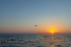 silhuett av driven paraglider stigande flyg över de hav mot underbar orange solnedgång himmel. skärmflygning - rekreations och konkurrenskraftig äventyr sport. foto