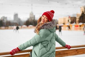 skön härlig medelålders flicka med lockigt hår värma vinter- jackor står is rink bakgrund stad fyrkant. foto