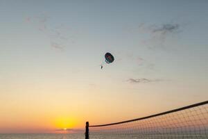 silhuett av driven paraglider stigande flyg över de hav mot underbar orange solnedgång himmel. skärmflygning - rekreations och konkurrenskraftig äventyr sport. foto