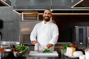 stilig ung afrikansk kock stående i professionell kök i restaurang framställning en måltid av kött och ost grönsaker. foto