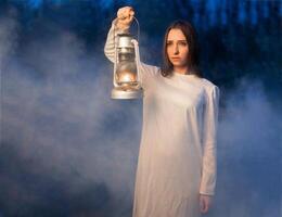 mystisk mystisk flicka i en mörk natt skog med en fotogen lampa i henne händer foto