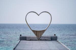 trä- hjärta formad stol ser genom de hav för par, hav bakgrund. foto