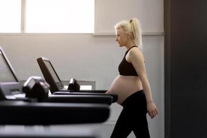 gravid kvinna Träning löpband maskin i Gym konditionsträning övningar på löpning simulator foto