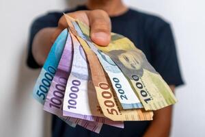 en man i svart kläder innehav de indonesiska pengar. indonesiska rupiah sedlar. foto