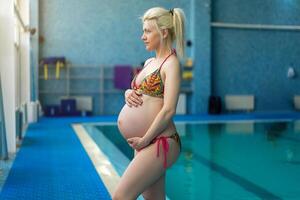 gravid kvinna stående inomhus swiming slå samman kram stor mage foto