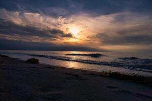 solnedgång, upplyst hav. sandig strand i de förgrund. ljus vågor. baltic hav foto