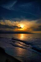 solnedgång, upplyst hav. sandig strand i de förgrund. ljus vågor. baltic hav foto