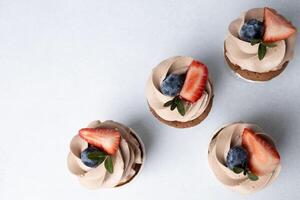topp se av choklad muffins med grädde ost glasyr, jordgubb och blåbär på ljus bakgrund foto