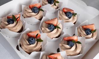 grupp av choklad muffins med grädde ost glasyr, jordgubb och blåbär i låda foto