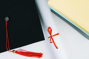 en svart fyrkant examen hatt med en röd tofs lögner på en diplom och en stack av böcker. utbildning begrepp foto
