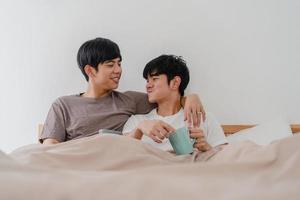Asiatiska homosexuella män par pratar ha en fantastisk tid i moderna hem. ung asien älskare manlig glad slappna av vila dricka kaffe efter vakna medan liggande på sängen i sovrummet hemma på morgonen koncept. foto