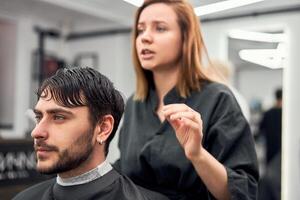 stilig blå ögon man Sammanträde i barberare affär. hårstylist frisör kvinna skärande hans hår. kvinna barberare. foto