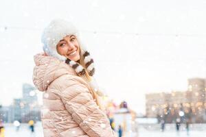 Lycklig vinter- tid i stor stad charmig flicka stående gata klädd rolig fluffig hatt. njuter snöfall, uttrycker positivitet, leende till kamera foto