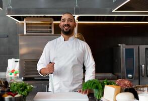 stilig ung afrikansk kock stående i professionell kök i restaurang framställning en måltid av kött och ost grönsaker. foto