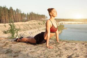 ung kvinna i röd sport topp praktiserande yoga i skön natur. meditation i morgon- solig dag foto