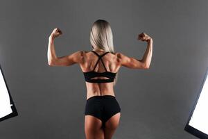 stark atletisk kvinna kondition modell Framställ tillbaka muskler, triceps, latissimus över svart bakgrund. studio skytte foto