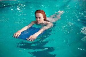 skön ung rödhårig caucasian flicka simmar i de inomhus- simning slå samman. friska livsstil. foto
