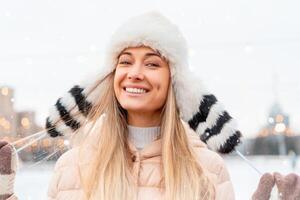 medium skjuta porträtt av romantisk europeisk lady bär lång eleganta vinter- jacka och rolig fluffig hatt i snöig dag. utomhus- Foto av inspirerad blond kvinna njuter vinter- stad.