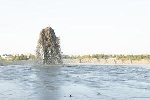 en stor fontän av vatten blandad med sand den där takter från en metall rör mot en blå himmel. sand brytning. foto