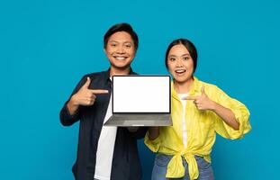 Lycklig asiatisk par pekande på en bärbar dator skärm med en tom visa foto