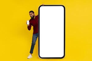 positiv indisk kille stående förbi stor telefon med vit skärm foto