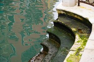 sten trappa täckt med alger längs en kanal under låg tidvatten i Venedig i Italien. grön kanal vatten. sjunkande Venedig. foto