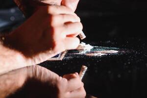 stänga upp av ung läkemedel -handlare sniffa läkemedel genom rullad ett hundra dollar räkningen från telefon skärm. manlig missbrukare passerade ut efter kokain överdos på tabell. missbruk och ämne missbruk begrepp. foto