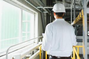 leende och Lycklig anställd. industriell arbetstagare inomhus i fabrik. ung tekniker med vit hård hatt. foto