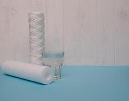 vatten filter. kol patroner och en glas på en vit blå bakgrund. hushåll filtrering systemet. foto