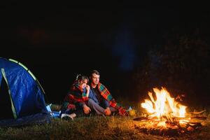 ung par har en resten på bål bredvid läger och blå turist tält, dricka te, njuter natt himmel. de begrepp av aktiva rekreation och resa med en tält foto