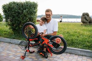 Lycklig far och hans son har roligt tillsammans på de grön parkera, fixering cykel tillsammans. fars dag. foto