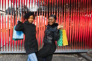 två afro amerikan kvinnor vänner i de stad på en handla resa bärande färgrik handla påsar. foto