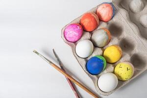 färgrik målad påsk ägg på en kartong bricka med måla borstar på en vit bakgrund. foto