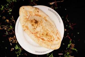 tandoori Smör naan eras i maträtt isolerat på mörk bakgrund topp se av indisk kryddor mat foto