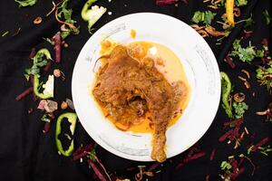 kyckling steka ben eras i maträtt isolerat på mörk bakgrund topp se av indisk kryddor mat foto
