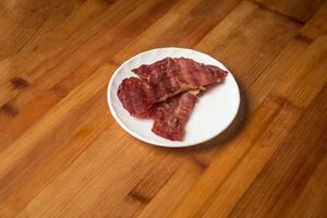 nötkött bacon skiva eras i tallrik isolerat på trä- tabell topp se av indisk mat foto