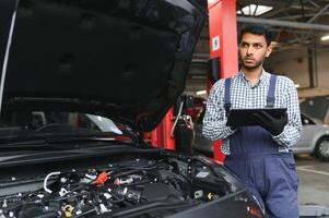 man bil tekniker mekaniker reparation bil problem av motor, under systemet kontroll detalj, använder sig av läsplatta dator för underhåll och fixering i bil garage. foto