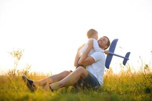 Lycklig far barn ögonblick. far piggybacking hans pojke på solnedgång medan han är spelar med leksak plan. foto
