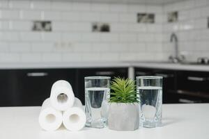 en glas av rena vatten med osmos filtrera, grön blomkruka och patroner på vit tabell i en kök interiör. begrepp hushåll filtrering systemet. foto