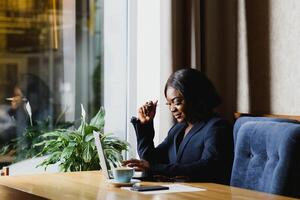 hård arbete ser till Framgång. koncentrerad ung afrikansk kvinnor arbetssätt på bärbar dator medan Sammanträde på arbetssätt plats foto