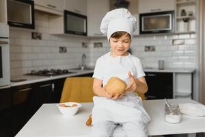 pojke i laga mat hatt Sammanträde på en kök disken. liten pojke i kök foto