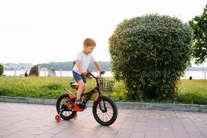 barn på en cykel på asfalt väg i tidigt morgon. liten pojke lär till rida en cykel i de parkera. Lycklig leende barn, ridning en cykling foto